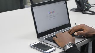person typing into Google on laptop on desk