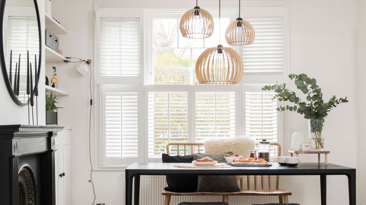 white dining area with black table, wooden bench and statement lighting