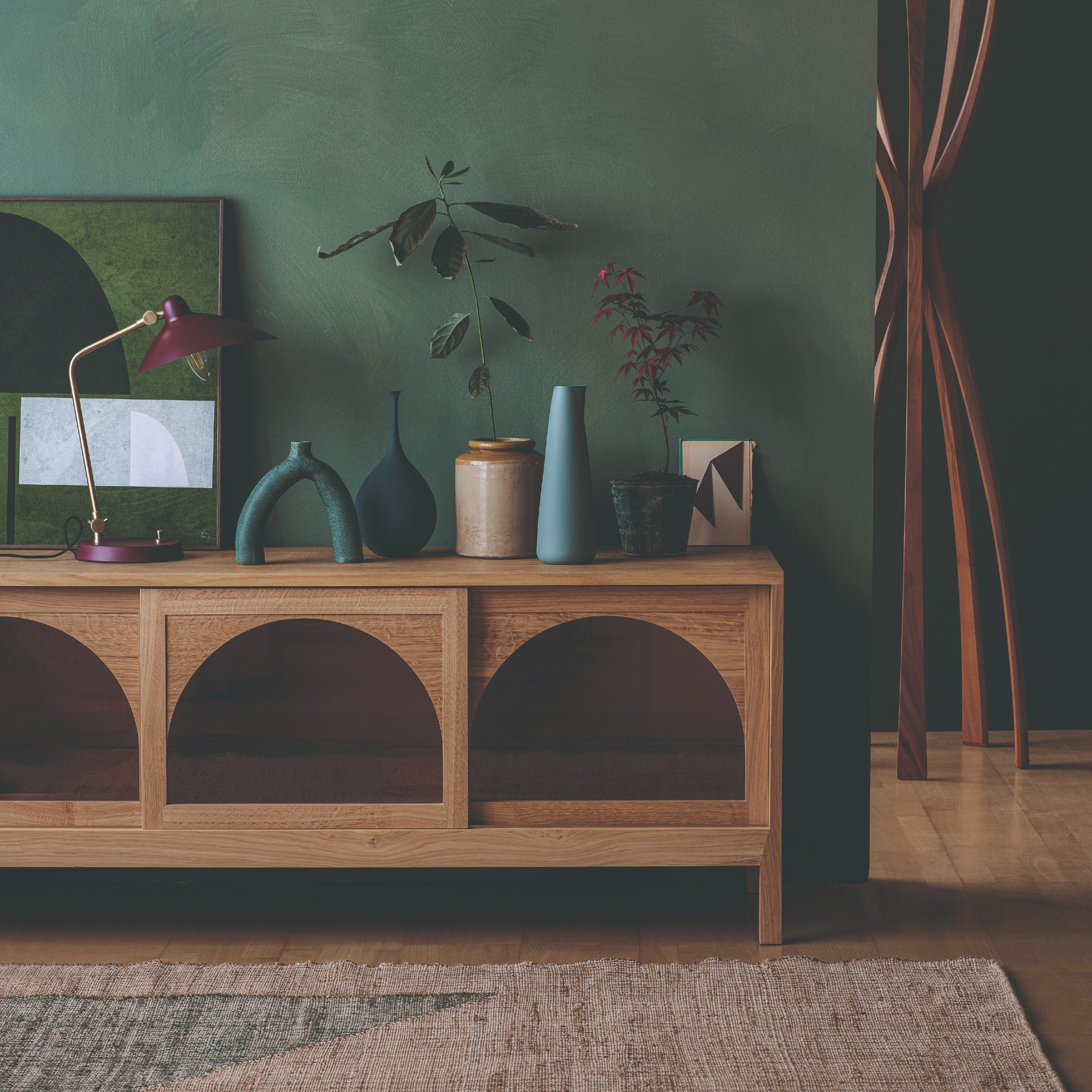 A room painted in dark green with a sideboard displaying a framed artwork leaning against the wall