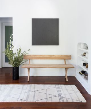 Modern entryway with white wall, dark floor and wood bench