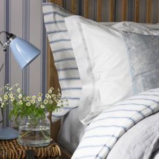 Bed with pillows, blue and white striped bedding and flowers on nightstand