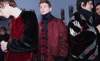 Three male models stood wear coats - two in fluffy jackets and one in red bomber jacket