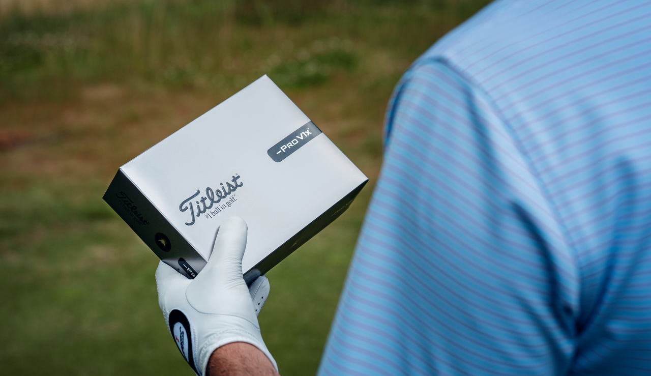 A golfer holds a box of Titleist Pro V1x Left Dash golf balls