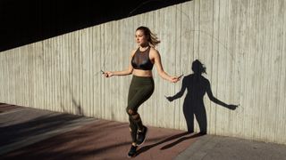 Woman jumping rope outdoors against a white wall