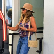 Jennifer Aniston opens a car door wearing a plaid sleeveless top, baggy blue jeans and brown flip-flops sandals.