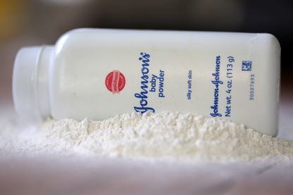 A Johnson & Johnson baby powder bottle sits on its side in a pile of white powder