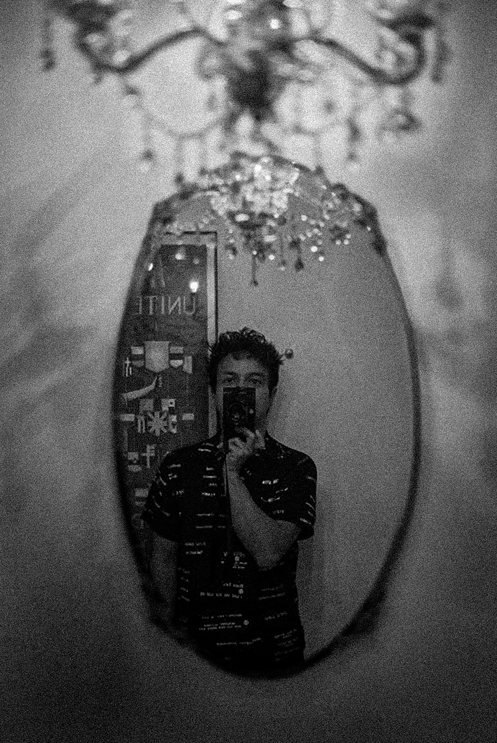 a black and white photo, a self portrait in a mirror with a chandelier above