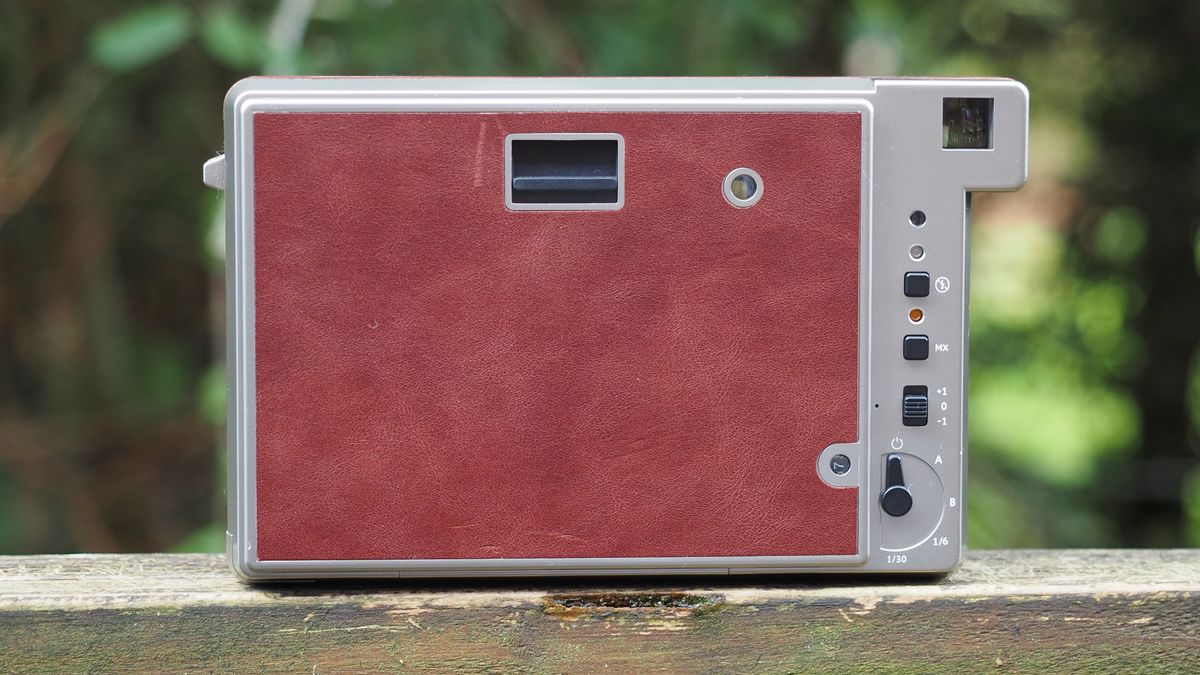 Lomo'Instant Wide Glass camera, sitting on a wooden surface, outdoors against a woodland background