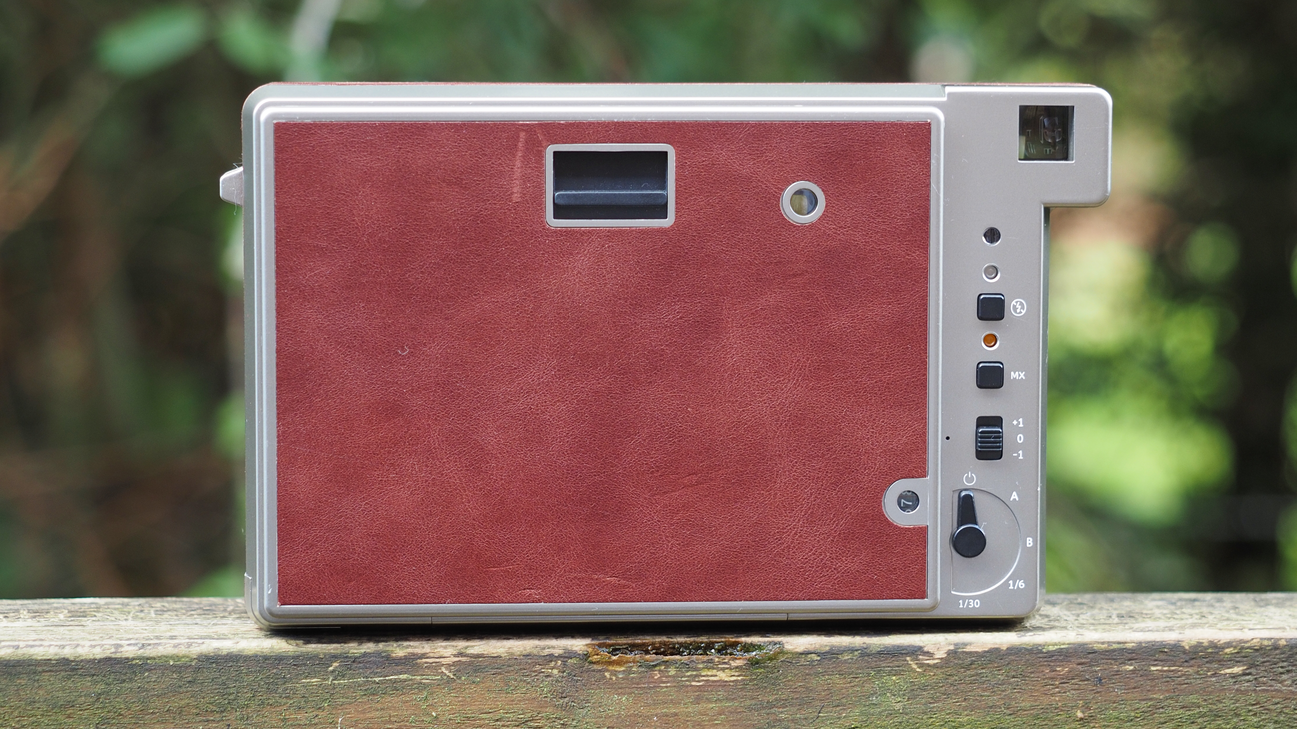 Lomo'Instant Wide Glass camera, sitting on a wooden surface, outdoors against a wooded background