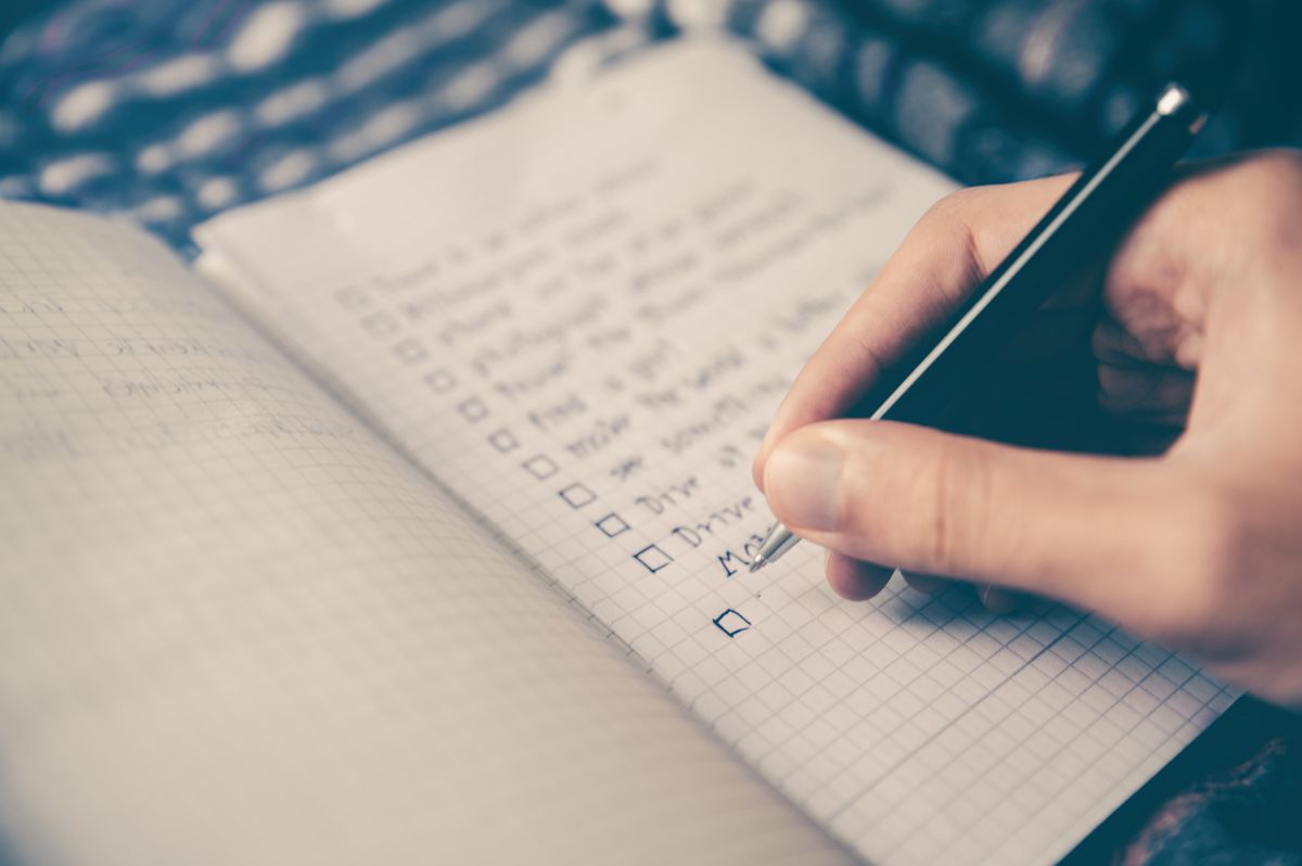 A hand is using a pen to check off various tasks on a list of goals on a notebook