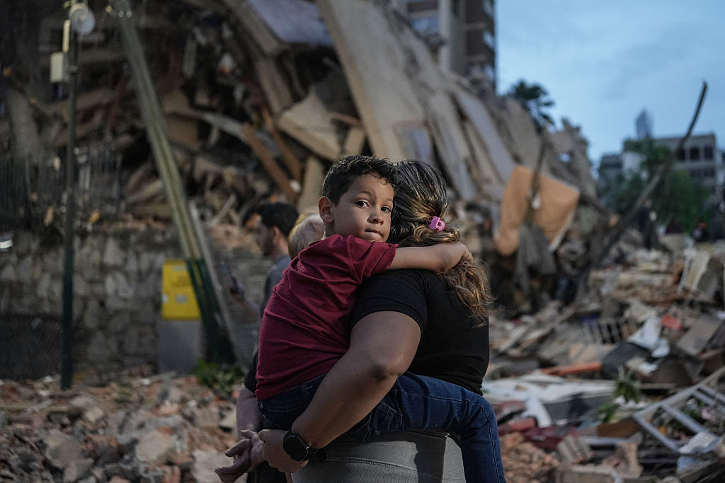 People walk past a collapsed building following an earthquake in Caracas on June 25, 2026. Powerful twin earthquakes have killed 32 people and injured more than 700, the nation's interim president said on June 25, after the massive shocks collapsed entire buildings and sent people running in panic. (Photo by Manaure QUINTERO / AFP)