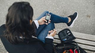 A woman sits on a park bench to use a glucose meter