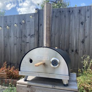 Woody pizza oven infront of a fence with festoon lights