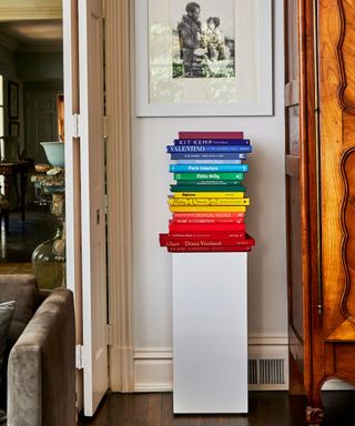 An entryway with a white pedestal holding a rainbow-colored stack of books