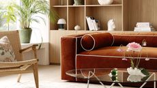 living room with timber joinery, windowsill with potted plant, woven armchair with a cushion, orange velvet sofa with white contrast piping, and a glass coffee table styled with glass objects and a vase with a rose in it