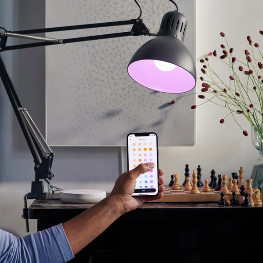 Hand holding the DIRIGERA hub app to control light above