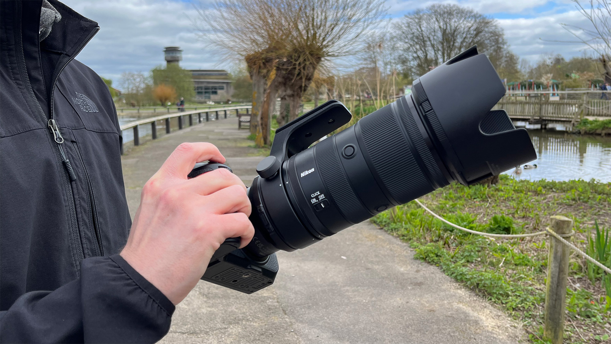 Mike Harris holding Nikon Z 70-200mm f/2.8 VR S II by a lake with vegetation and trees in the background