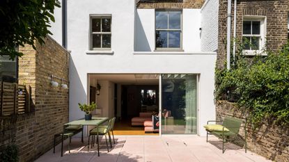 Image of the back of a white townhouse with a terracotta tile. The sliding glass doors are open and there is green outdoor furniture on the patio.