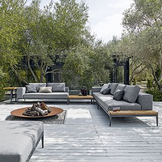 Grey outdoor sofa with a bonfire place under the trees