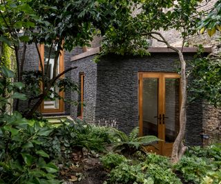 small extensions clad in dark stone and surrounded by trees