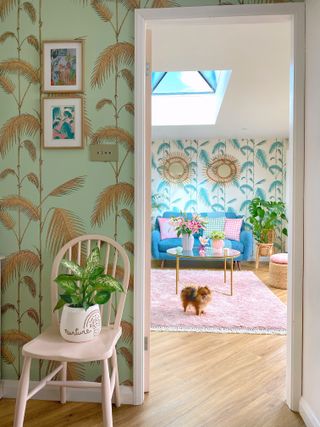 Gold leaf and green tropical wallpaper in hallway sets off blue wallpaper in living room with pink floor rug and bright furnishings