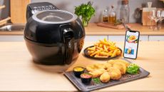 Tefal ActiFry Genius+ air fryer on wooden kitchen top surrounded by food