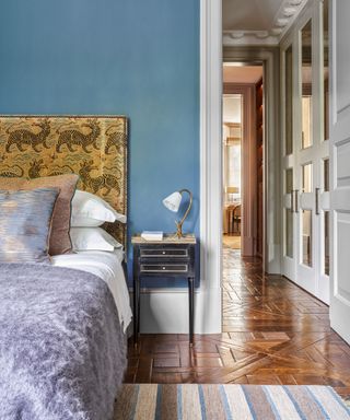 Bedroom decorated in blue with wooden parquet flooring, double bed with grey and white bedding and view through the doorway to the landing.