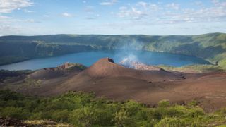 A photo taken from the caldera's rim showing smoke coming from a volcanic cone and the crater lake in the background