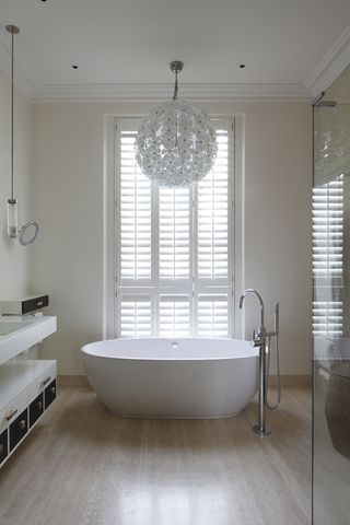 A stylish white bathroom with a white bath below a large window and spherical ceiling light
