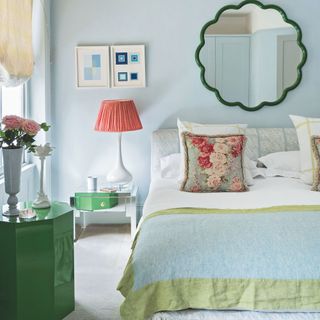 Light blue bedroom with a green mirror on the wall, pink lampshade, and bold accessories