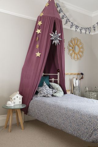 Child's room with beige walls, burgundy bed canopy and blue and pink floral pattern bed linen