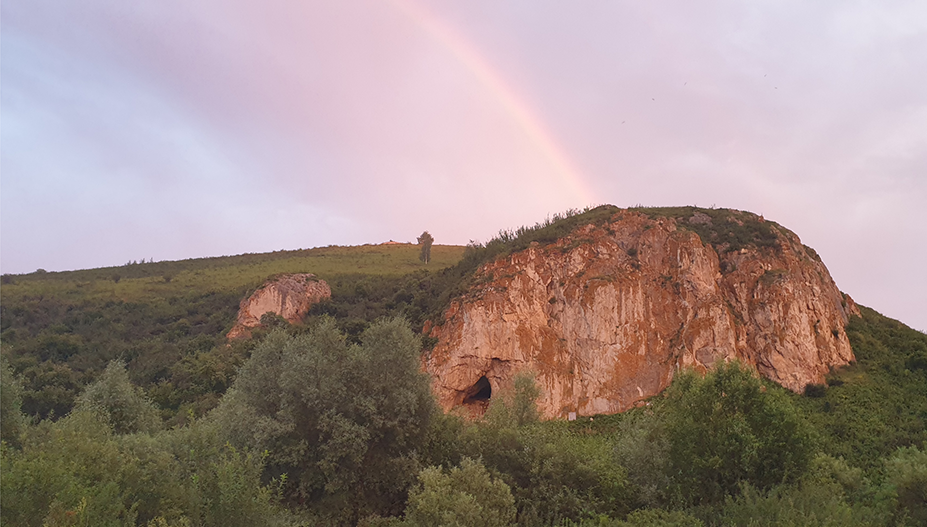 View of Chagyrskaya Cave with a rainbow and pale purple sky.
