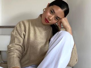 fashion influencer posing in gold earrings, red lipstick, neutral turtleneck sweater and white jeans