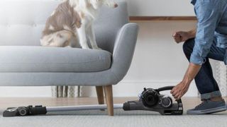 The Hoover ONEPWR Blade+ fully extended under a sofa with a dog sitting on top