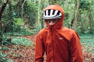 Orange Rapha Explore Goretex jacket with the hood stretched over a helmet