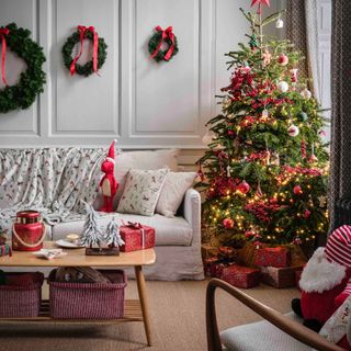 living room with Christmas tree, three wreaths on the wall behind sofa, carpet, mid century modern coffee table, presents, white, red and green theme