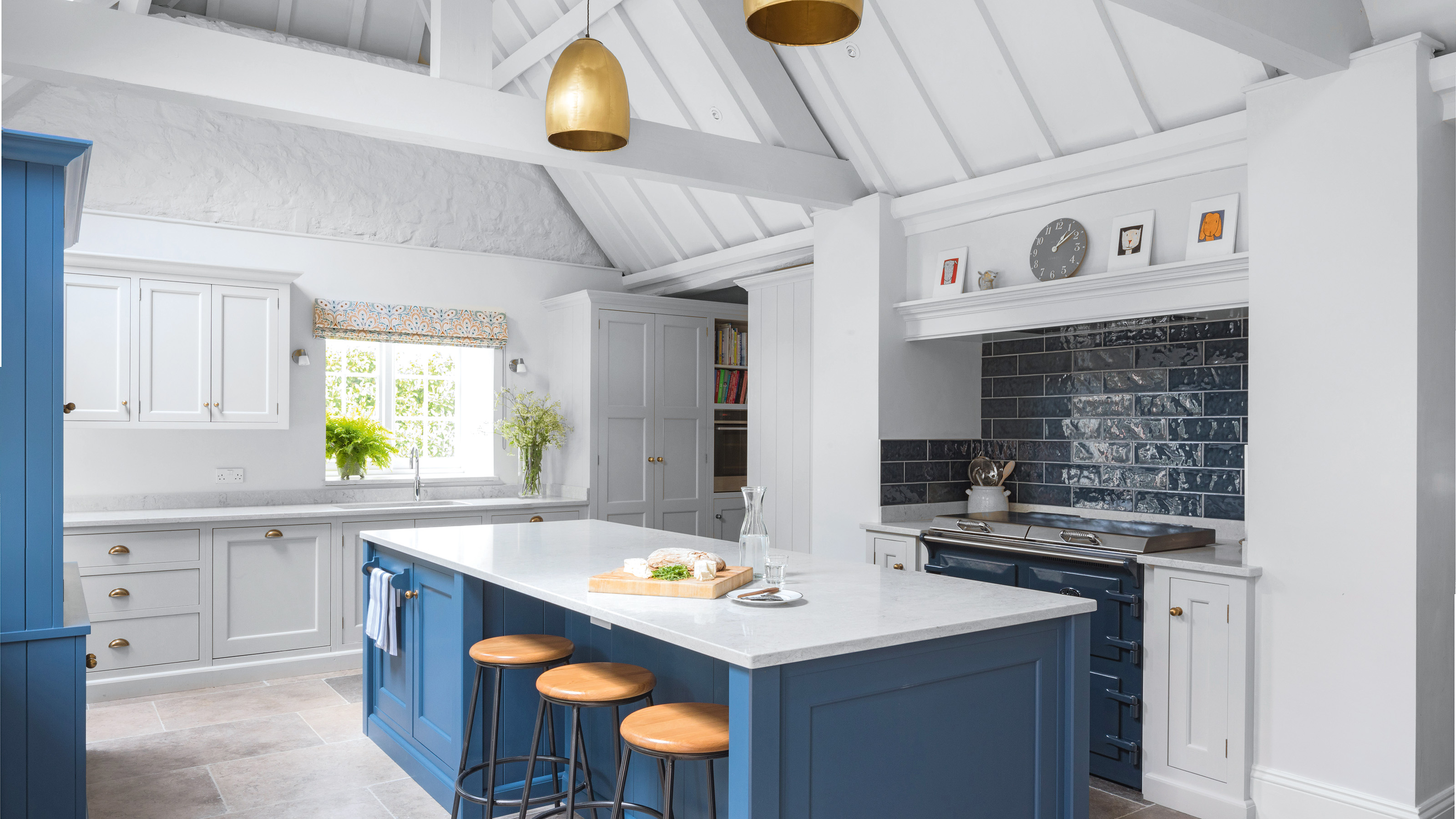 white kitchen with blue island with quartz worktop in the centre with three wooden stools and navy range cooker and metro tiles