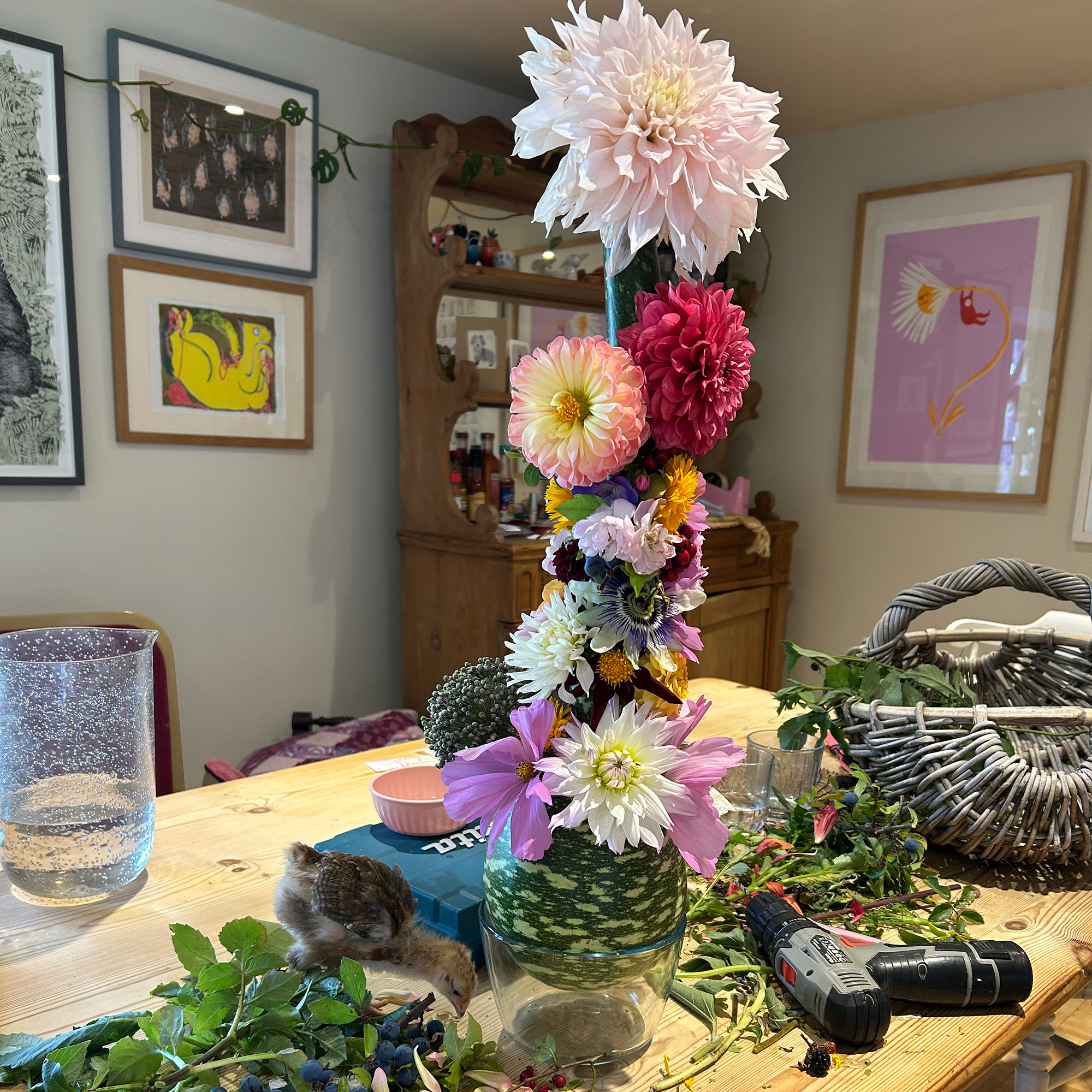 Wooden kitchen table with small bird beside glass vase filled with tower of dahlias