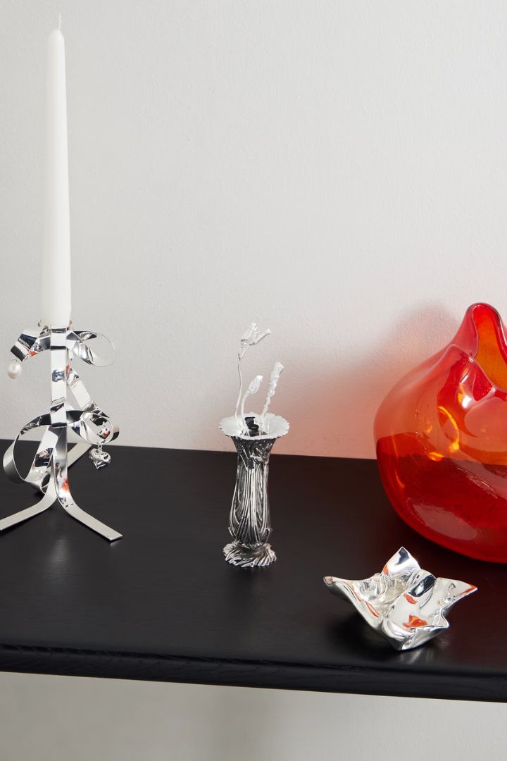 Set of Two Silver-Plated Flower Ornaments sitting on a black shelf alongside other chrome and fluted colorful glass sculptures.