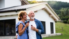 A happy older couple drink wine outside their house and contemplate retirement.