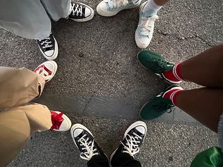 five people are wearing various converse shoes while forming a star with their feet