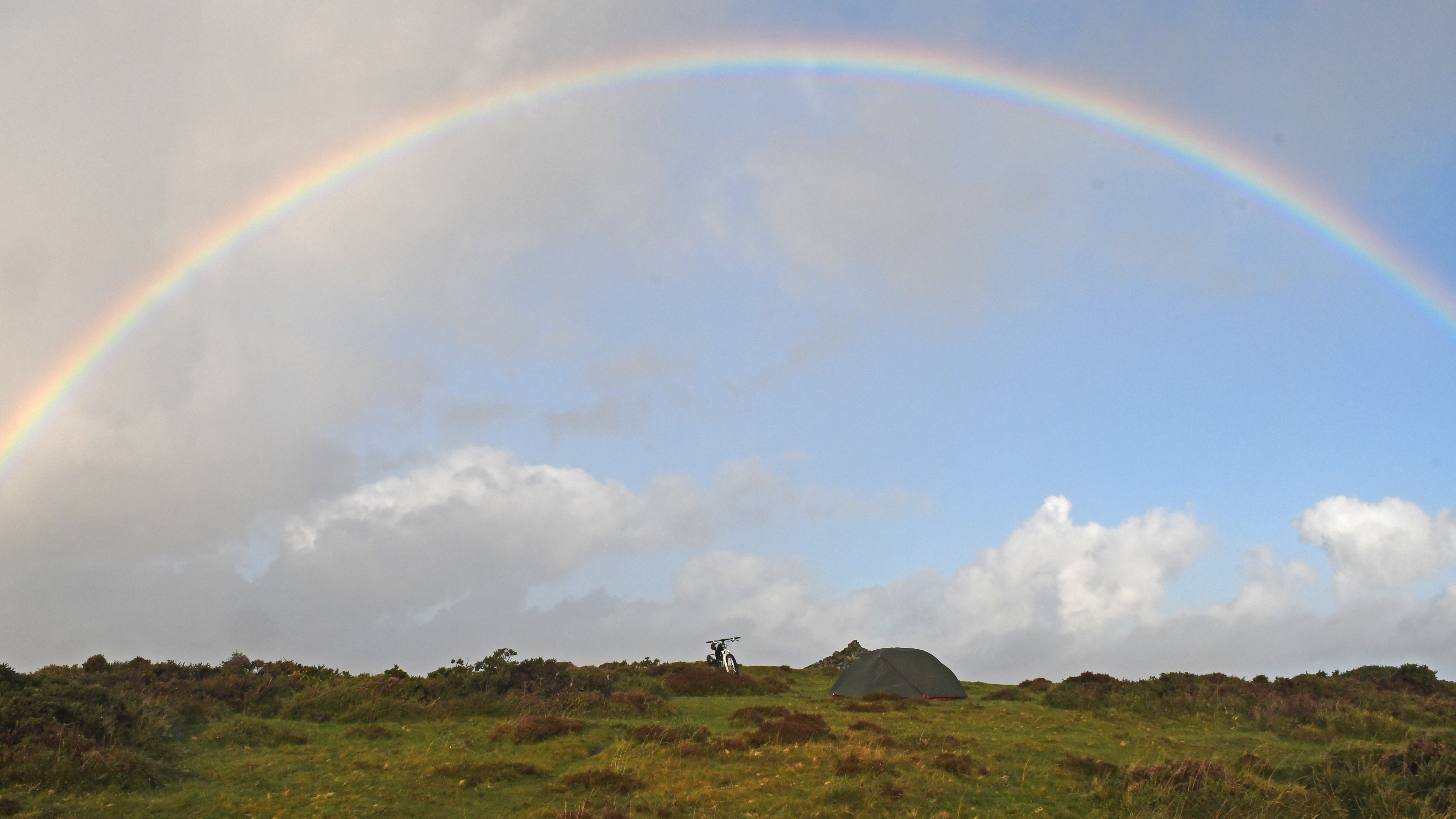 A Hubba Hubba Bikepacking tent pitched on Dartmoor, with a rainbow arcing over the tent and a mountain bike
