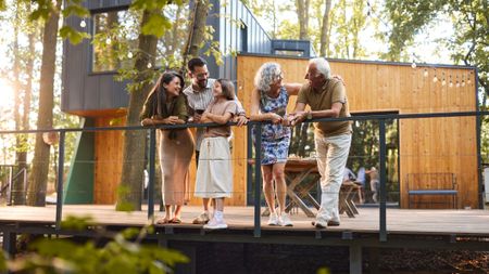 A happy multi-generation family relax on the deck of a modern home in the woods. 
