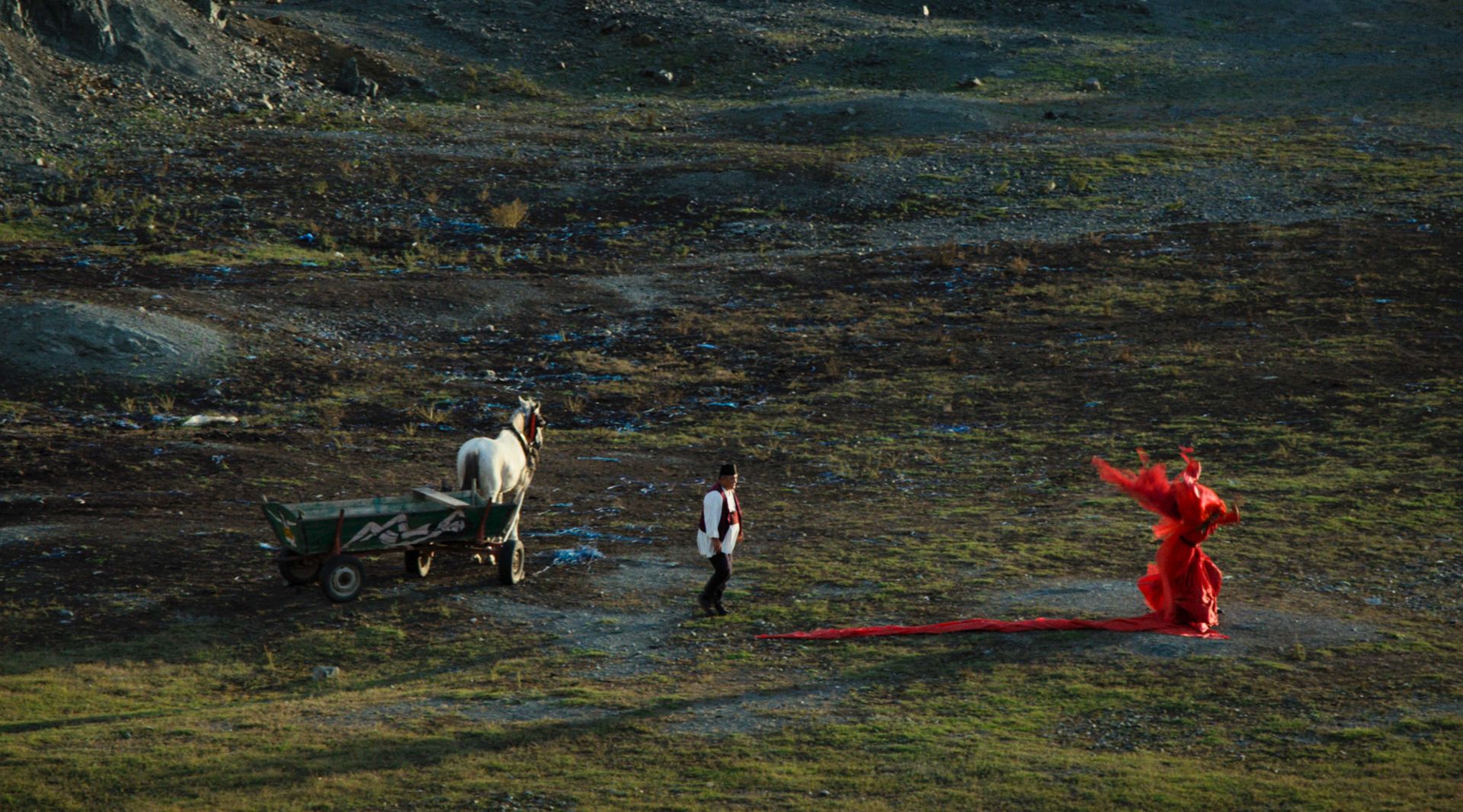 film still of figure in red on plain with horse and cart