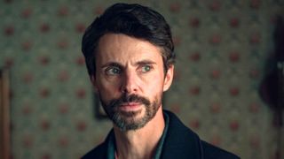 Matthew Goode stares out of a window to his left