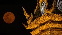 Photo of a red moon and the golden clock tower of Chiang Rai province the northern part of Thailand.