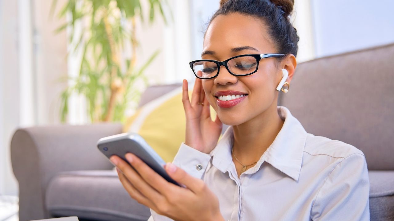 A young woman smiles as she listens to something on her smartphone while wearing earbuds.