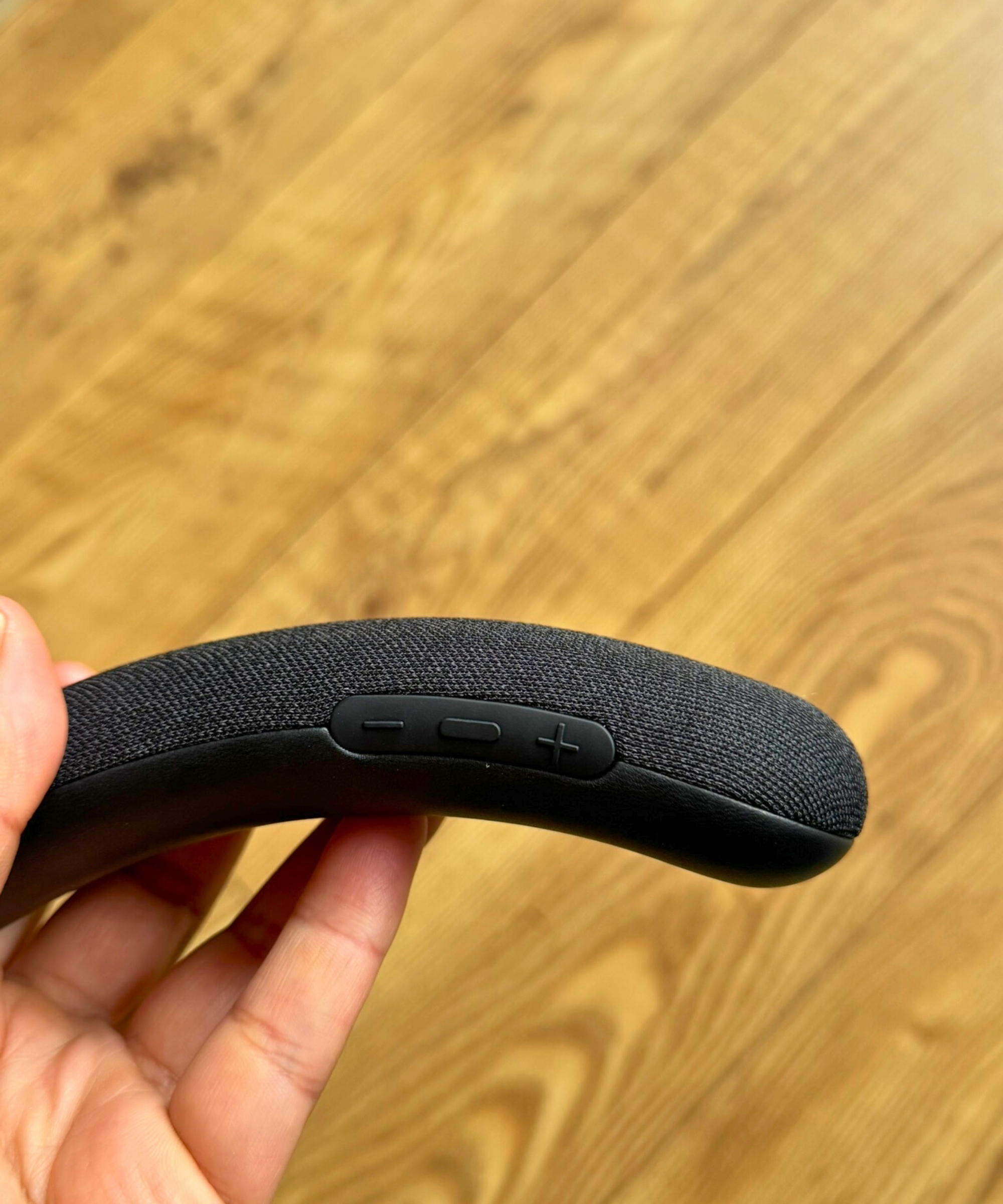 Hand holding the Sony BRAVIA Theatre U, showing volume and control buttons, above wooden floor.