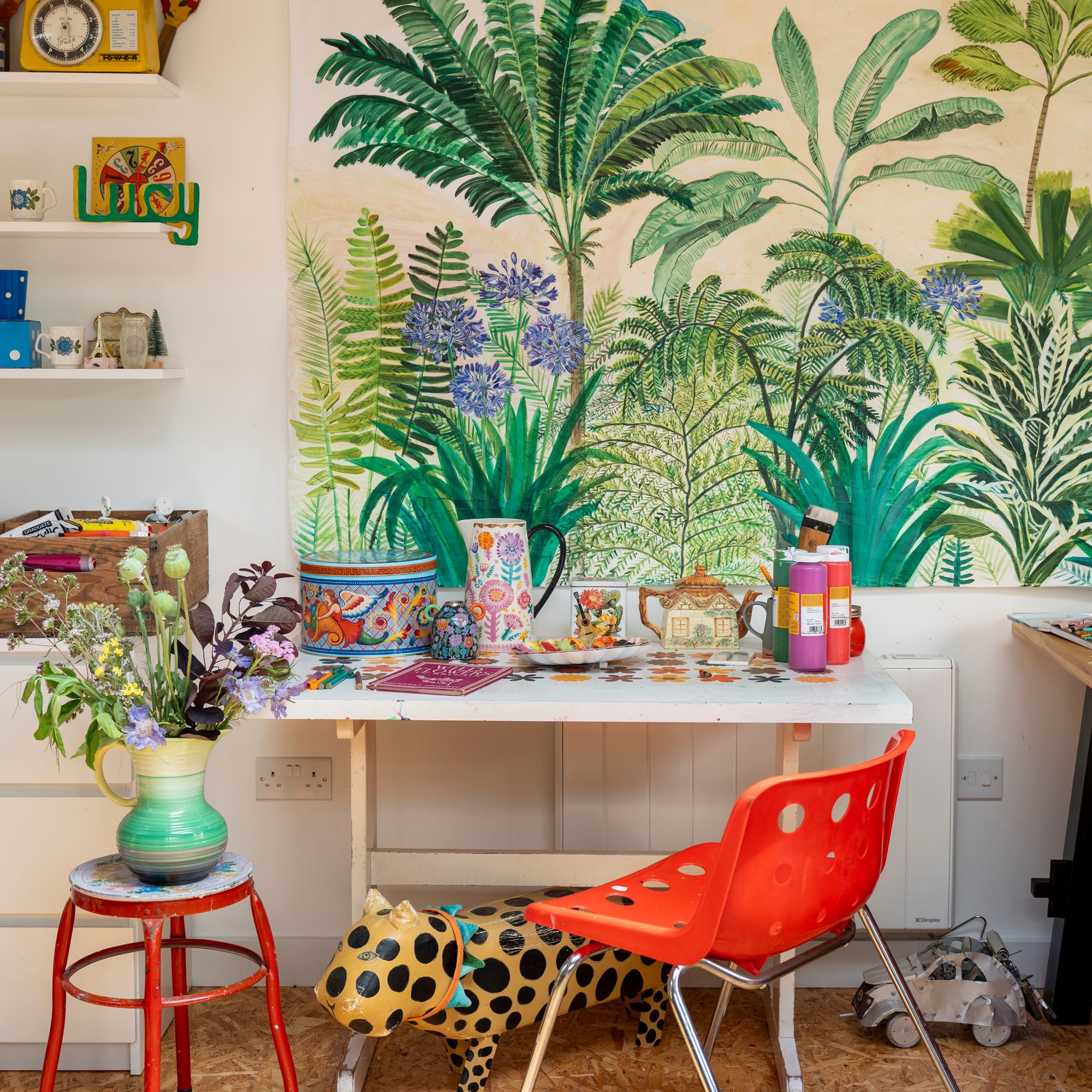 art studio desk with a colourful hand-painted jungle mural on the wall and a red chair