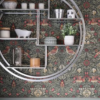patterned green wallpaper with silver shelving unit and small plants and ornaments